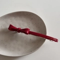 Détail d'une barrette nœud rouge avec gravure dorée dans un plat en céramique - Rouge