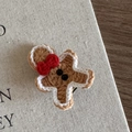 Détail d'une barrette bonhomme en pain d'épices tricotée à la main avec un nœud rouge - Bonhomme en pain d'épices