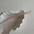 Detail der Haarnadel aus Acetat mit handgefertigtem Logo auf einer Keramikschale in Muschelform - Transparentes Weiß