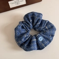 Detail eines blauen Tweed-Haargummis mit klassischem Knopfakzent und reicher Webstruktur - Blau Tweed Knopf Stil