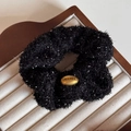 Detail of black plush scrunchie with silver sparkles and a golden oval metal logo plate - Black Scrunchie