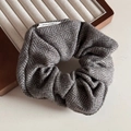 Macro detail van grijze wollen scrunchie met visgraatpatroon en elegant stoffen merklabel - Khaki