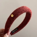 Close-up of burgundy wool headband with golden oval buckle and engraved lettering - Red