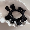 Dettaglio di un elastico per capelli nero con fiocco in tessuto su ceramica bianca - Nero