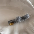 Macro view of grey knit bow hair clip with gold logo tag in a ceramic dish - Knit Knot Clip - Gray