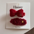 Détail de barrettes festives rouges avec broderie de nœud et strass sur carte de support - Ovale Pelucheux