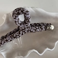 Détail de la pince à cheveux fleurie avec perle et étiquette en métal sur plateau coquillage - Pince à cheveux cintre / Floral Violet Café
