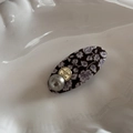 Détail de la pince à cheveux fleurie avec perle et logo en métal doré sur fond blanc - Short Oval Clip / Floral Violet Café
