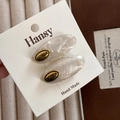 Detailed close-up of oval acetate hair clips with golden label and pearlescent texture - White