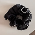 Détail d'un chouchou en organza noir avec bordure blanche et petite étiquette mode - Noir