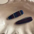 Detail of blue striped resin hair clip with smooth finish on a beige tray - Blue Purple