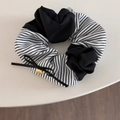 Détail d'un chouchou rayé noir et blanc avec nœud en soie et médaillon logo doré - Chouchou Patchwork Noir et Blanc