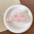 Dettaglio di molletta rosa chiaro con fiori blu su un piatto di ceramica bianco - Rosa