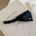 Détail d'une pince banane en satin noir avec tissu plissé et petite plaque dorée chic - Noir