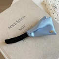 Détail d'une pince banane en satin bleu clair avec des ailes plissées et logo doré - Bleu