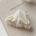 Detail of champagne satin hair clip with delicate white lace trim on textured book cover - Yellow Hair Claw