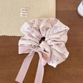 Détail d'un chouchou en mousseline fleurie rose avec un long nœud sur fond en bois - Rose