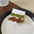 Gros plan de barrettes à cheveux en acétate vert olive et écaille sur carte d'affichage - Bleu Café Vert