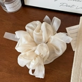 Close-up of cream organza hair scrunchie with long ribbons on a warm wooden surface - Off-white