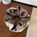 Detail eines Seidensatin-Scrunchies in Braun und Creme auf einer Holzoberfläche - Kaffee Mehrfarbig