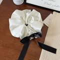 Détail d'un chouchou en satin blanc élégant avec un long ruban noir sur bois - Blanc Cassé