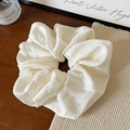 Close-up of cream pleated fabric scrunchie with sparkling rhinestones on wooden table - Off-white