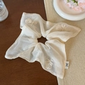 Dettaglio di scrunchie beige con ricamo di rose e logo del marchio su tavolo in legno - Cream Rose Embroidery (Cream Scarf Style)