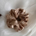 Close-up of champagne silk scrunchie with pleated texture on white fabric background - Orange