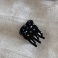 Close-up of a black acetate flower hair claw clip with colorful rhinestones on fabric - Black
