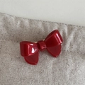 Detailed close-up of glossy red acetate bow hair clip on natural beige fabric texture - Hair Bow
