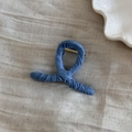 Dettaglio della molletta per capelli in denim blu su sfondo di tessuto beige chiaro - Stile Incrociato Blu Chiaro (Denim Avvolto - X Chiara)