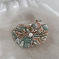 Detailed close-up of marble acetate orchid hair clip with pearl center on a white shell plate - Marble Orange Green