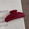 Close-up of a glossy dark red resin hair claw clip resting on a textured fabric book cover - Gold Glitter Red - Fan Shape