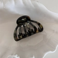 Detail of shell-shaped acetate hair claw clip with tortoiseshell texture on white tray - Mixed Green