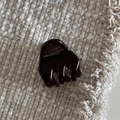 Detalle de una pequeña pinza para el cabello de acetato marrón sobre tela gris suave - Café oscuro