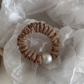 Detalle de coletero de tela brillante champán con elegante perla blanca grande central - Albaricoque