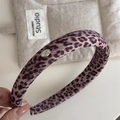 Detail van roze haarband met luipaardprint, luxe stoftextuur en zilveren logoplaatje - Roze Luipaard Hoofdband
