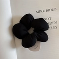 Close-up of black flower fabric scrunchie with a brand tag on a book page - Solid Black Style