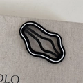 Detail einer wellenförmigen schwarz-weißen Haarklammer mit modernem Design auf Beigestoff - Schwarze Basis Weiße Linie - Wolke