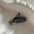 Vue macro montrant la texture en tweed gris et le nœud noir avec logo métallique sur le clip - Style Ovale Rond / Gris
