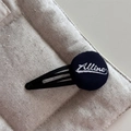Primo piano della clip BB in tessuto nero con ricamo Alline bianco su fondo beige - Blu navy