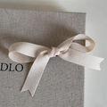 Primer plano de lazo de satén crema con textura mate en caja de lino rústica - Nudo Minimalista Color Sólido-Beige