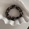 Dettaglio dell'elastico leopardato con trama a pieghe e perla nera su vassoio bianco - Stampa Leopardata Chiara Base