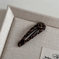 Nahaufnahme einer Haarspange mit Leopardenmuster und Metallverschluss auf beigem Stoff - Wassertropfenform / Leopard Umwickelte Träne