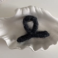 Primer plano de una pinza para el pelo de felpa negra en un plato de concha blanca - Cruzado / Negro