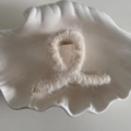 Detalle de pinza de pelo de felpa blanca crema con resorte metálico dorado en un plato - Cruzado / Beige