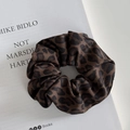 Primo piano di uno scrunchie leopardato in tessuto saia appoggiato su un libro bianco - Scrunchie / Leopardo Caffè