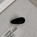 Detail of a black teardrop hair clip with golden France Handmade text on beige fabric - Black