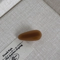 Detail view of a small amber brown teardrop hair clip on a textured linen background - Light Coffee