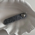 Vista dettagliata del fermaglio in tessuto grigio con cuore in metallo su un piatto a conchiglia - Cuore d'Argento Martellato Clip BB Lunga Grigio Argento